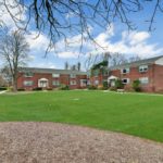 A large lawn with trees and buildings in the background.