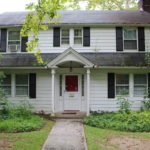 A white house with black shutters and red door.